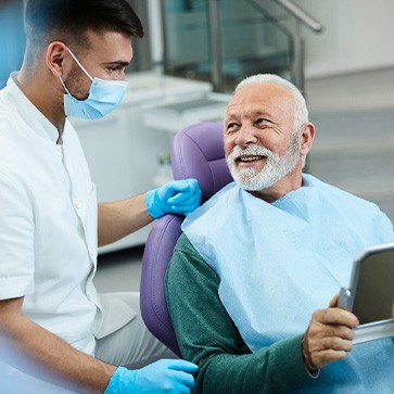 Senior patient looking at dentist while holding small mirror