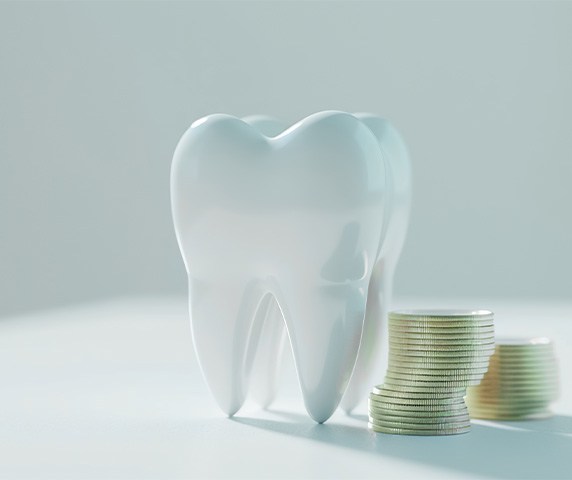 Large, shiny model tooth next to a pile of coins on a white surface with white background