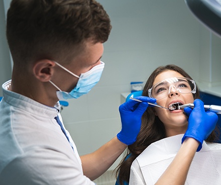 Woman with brown hair smiling into mirror as dentist points to her teeth