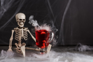 A skeleton sitting next to a glass of red alcohol on a foggy background